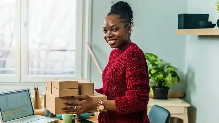 Propietaria de una empresa pequeña sosteniendo paquetes en su espacio de trabajo mientras sonríe